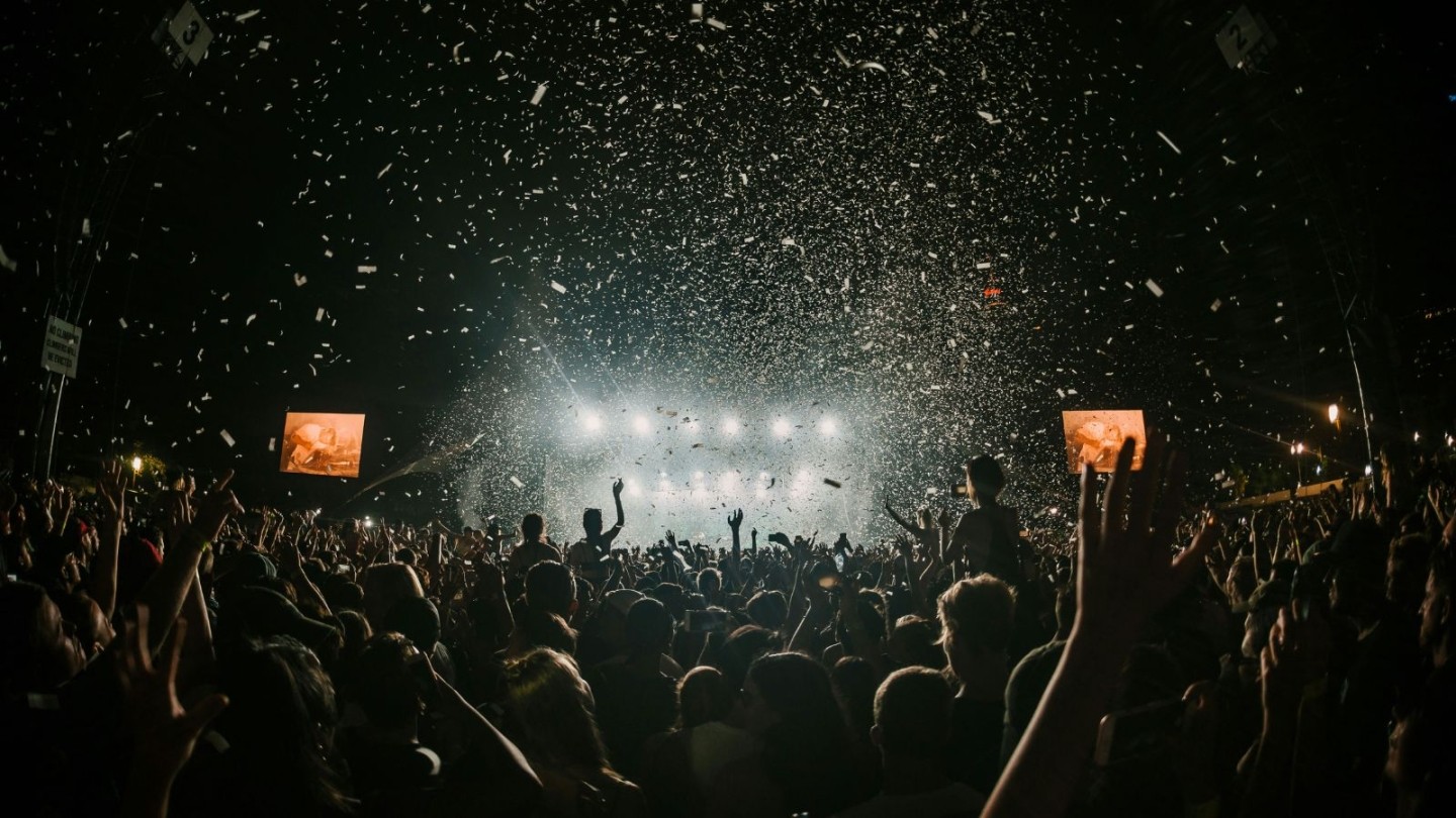 People at a festival at night with their arms in the air and white confetti falling down
