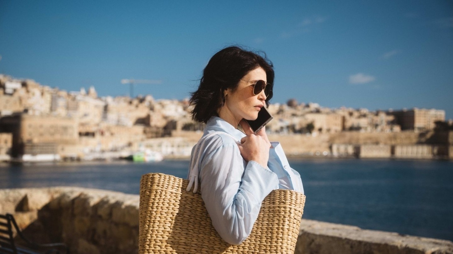 Intelligence officer holding a woven bag while standing by the waterfront in a European city, featured in Secret Service