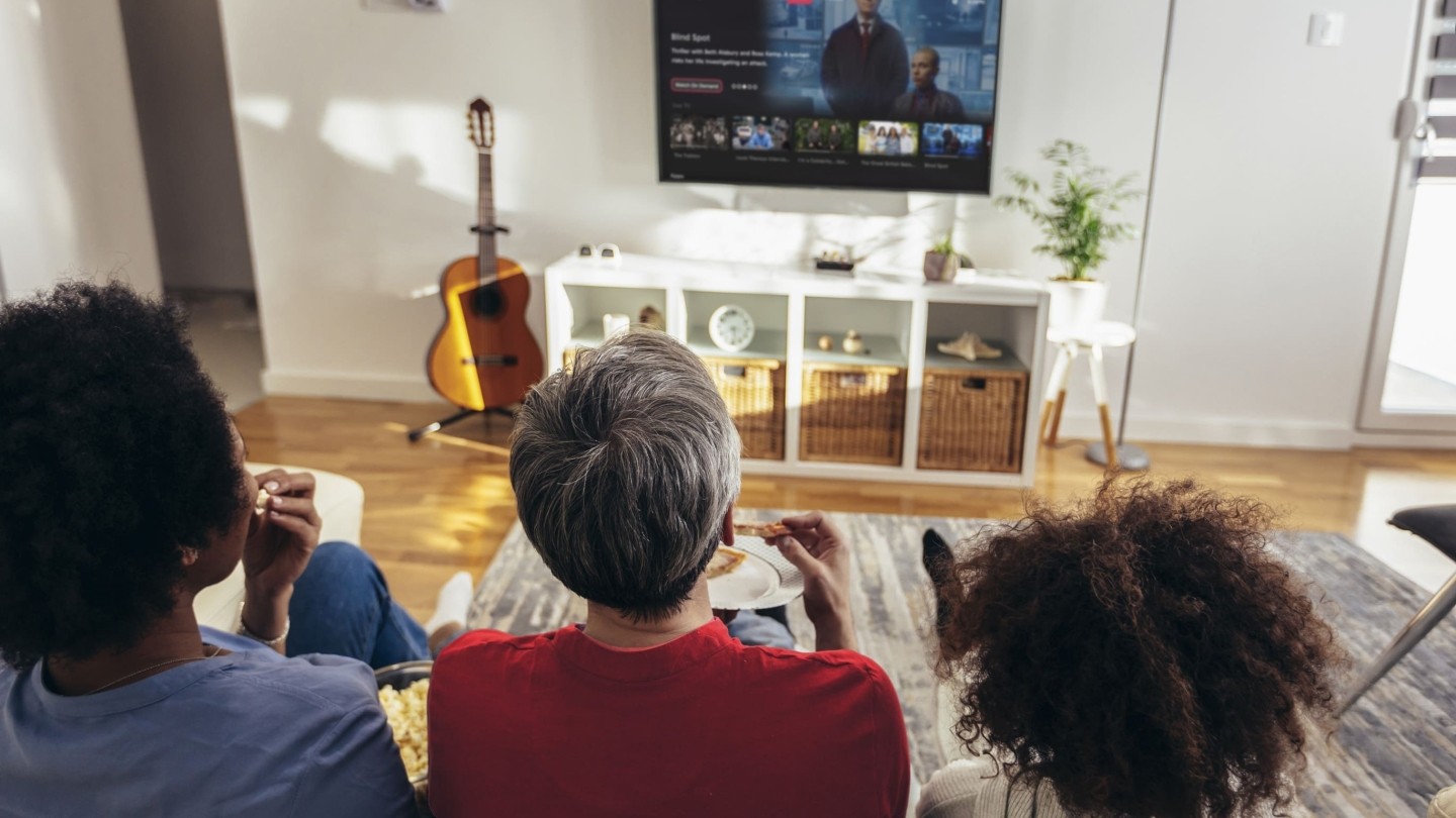 Three people sit watching a Freely TV in their living room