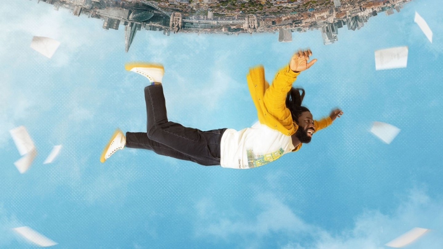 Upside down image of a man with a yellow jacket falling from a city into the sky. Key art for Dreaming Whilst Black.