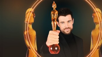 Person holding a golden award trophy in the foreground, framed by two stylised golden statuette figures and glowing circular light effects on a dark background