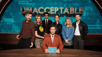 Six people pose on a television studio set in front of a large “UNACCEPTABLE” sign. One person sits at a desk holding a programme card while five others stand behind, framed by blue graphics and warm studio lighting. 