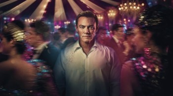 Luke Evans stood in the middle of a crowded scene with a circus tent in the background in the drama The Party