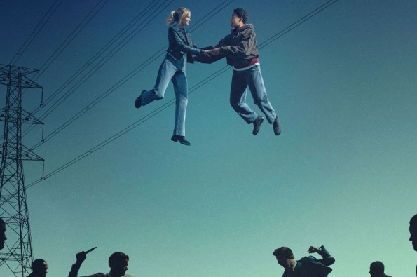 Two people suspended mid‑air while holding hands above a group of silhouetted figures, set against a clear sky with electricity pylons and overhead power lines in the background.