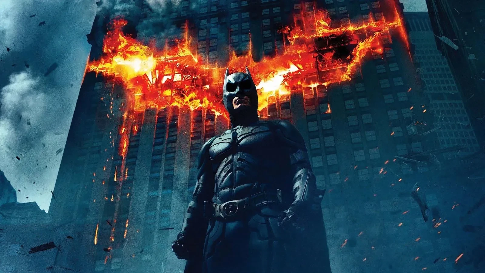 Batman stood against a burning building with flames in the shape of a bat