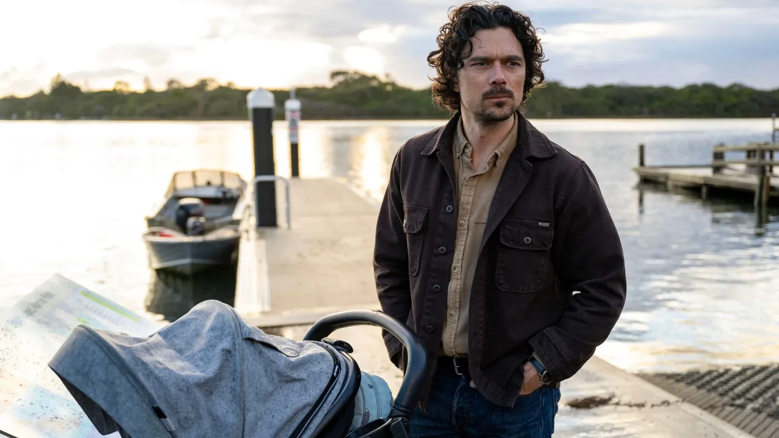 A man with curly hair stood on a pontoon with a pram