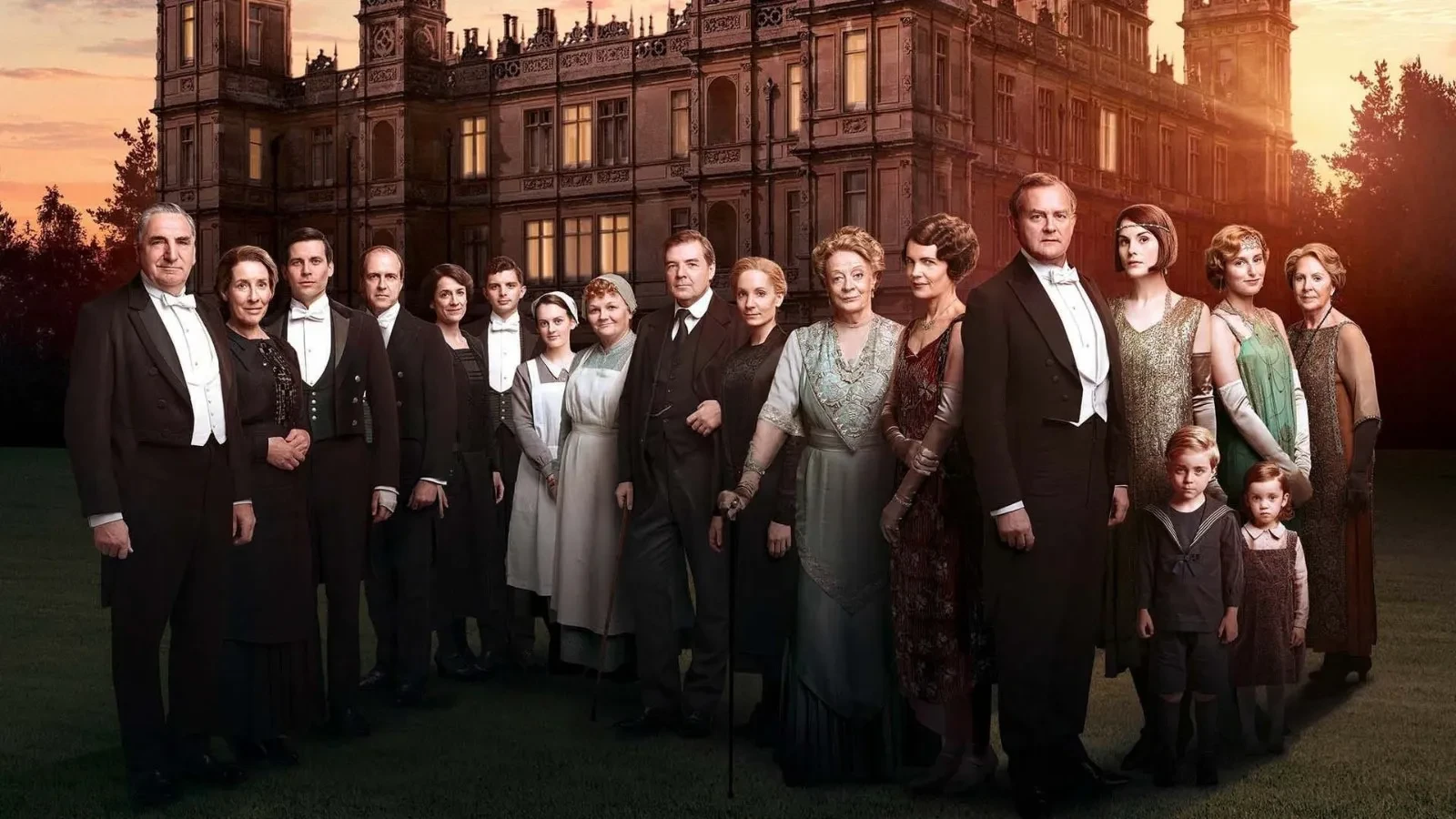 A large group of elegantly dressed individuals wearing formal evening attire and period costumes standing together on the lawn of a grand historic estate at sunset, with the stately manor house glowing warmly in the background, evoking a classic early‑20th‑century aristocratic setting.