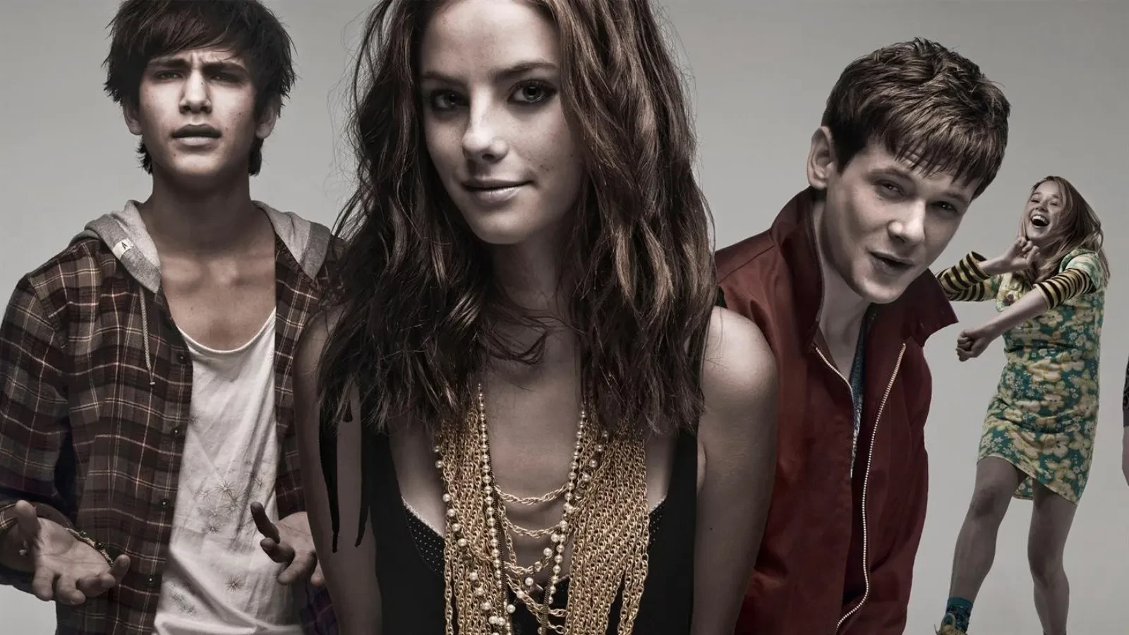 A group of young people dressed in edgy, contemporary clothing pose against a neutral studio background, featuring layered jewellery, casual streetwear and bold fashion choices, creating a raw, rebellious and youth‑culture aesthetic.