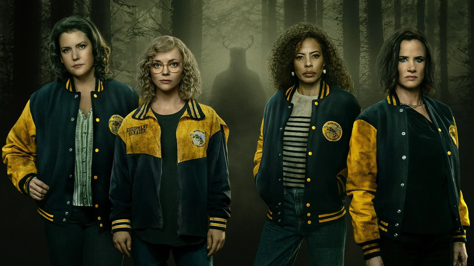 Four people wearing matching yellow-and-blue varsity jackets standing in a dark, misty forest, with a shadowy horned figure looming in the background
