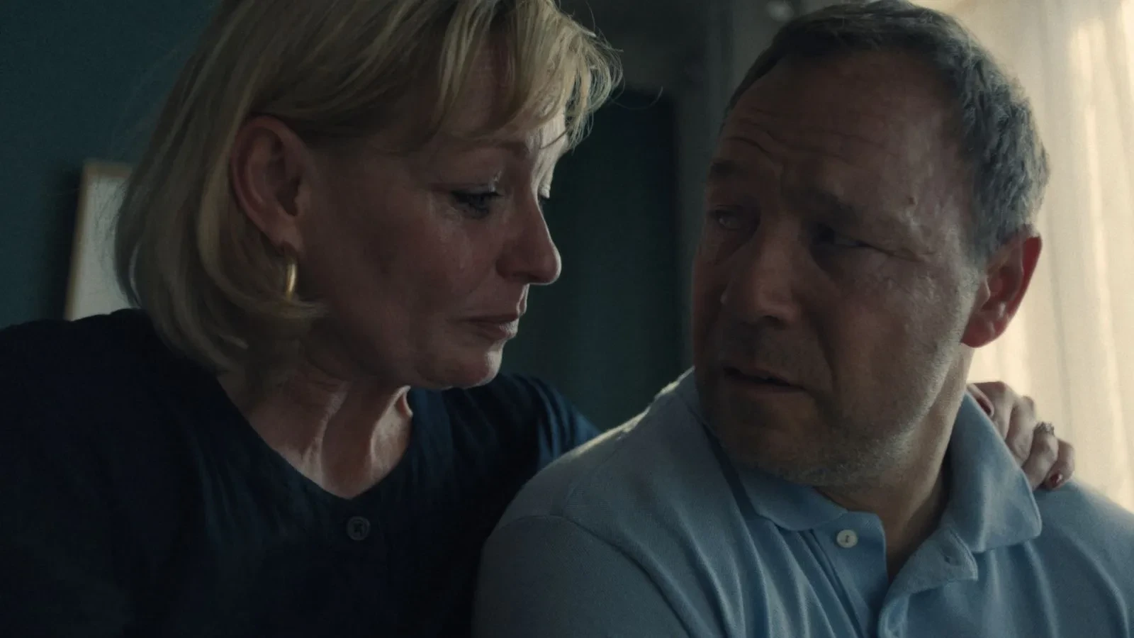 Two people sitting close together in a softly lit room, sharing a quiet moment at home.