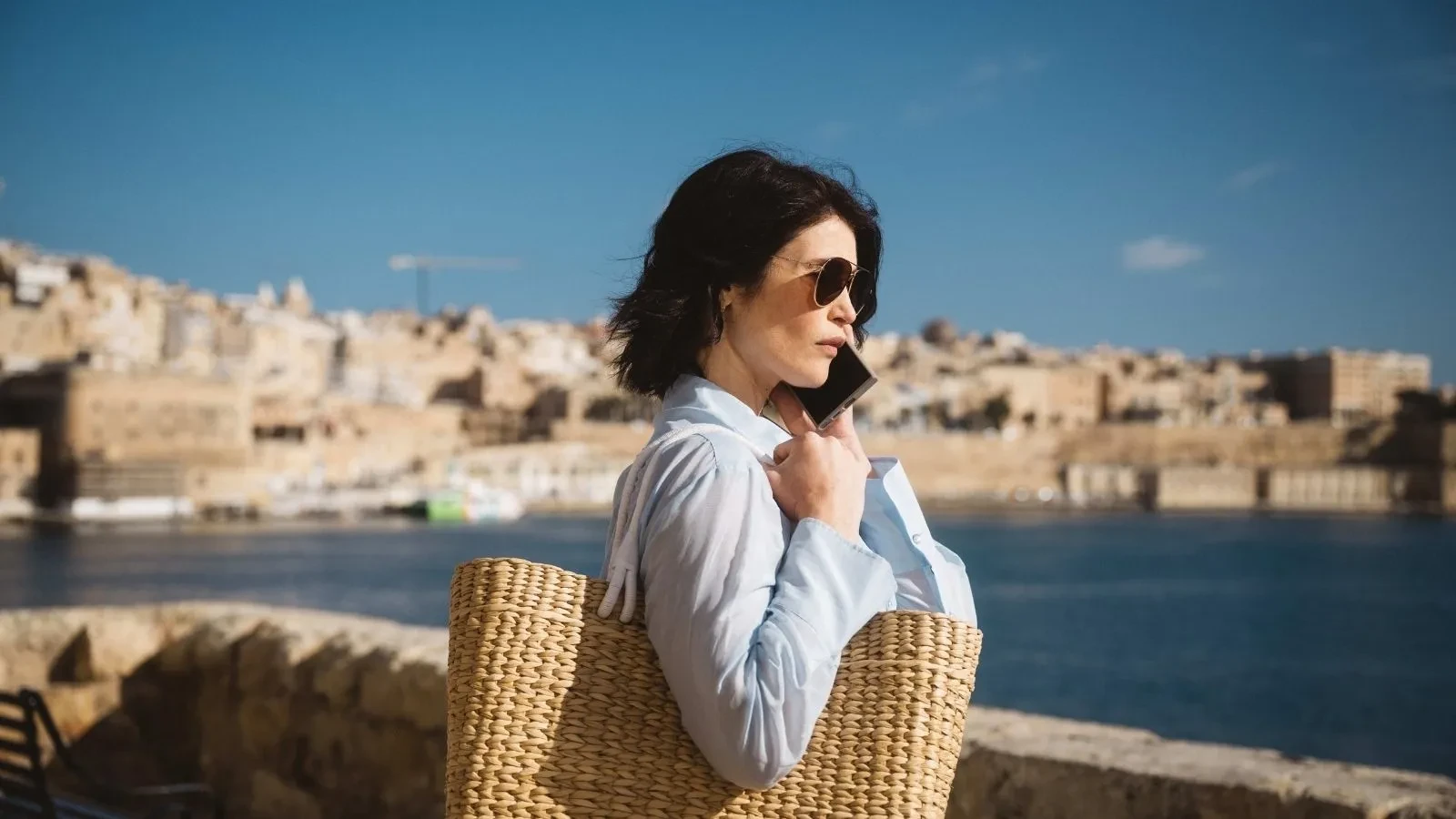 Intelligence officer holding a woven bag while standing by the waterfront in a European city, featured in Secret Service