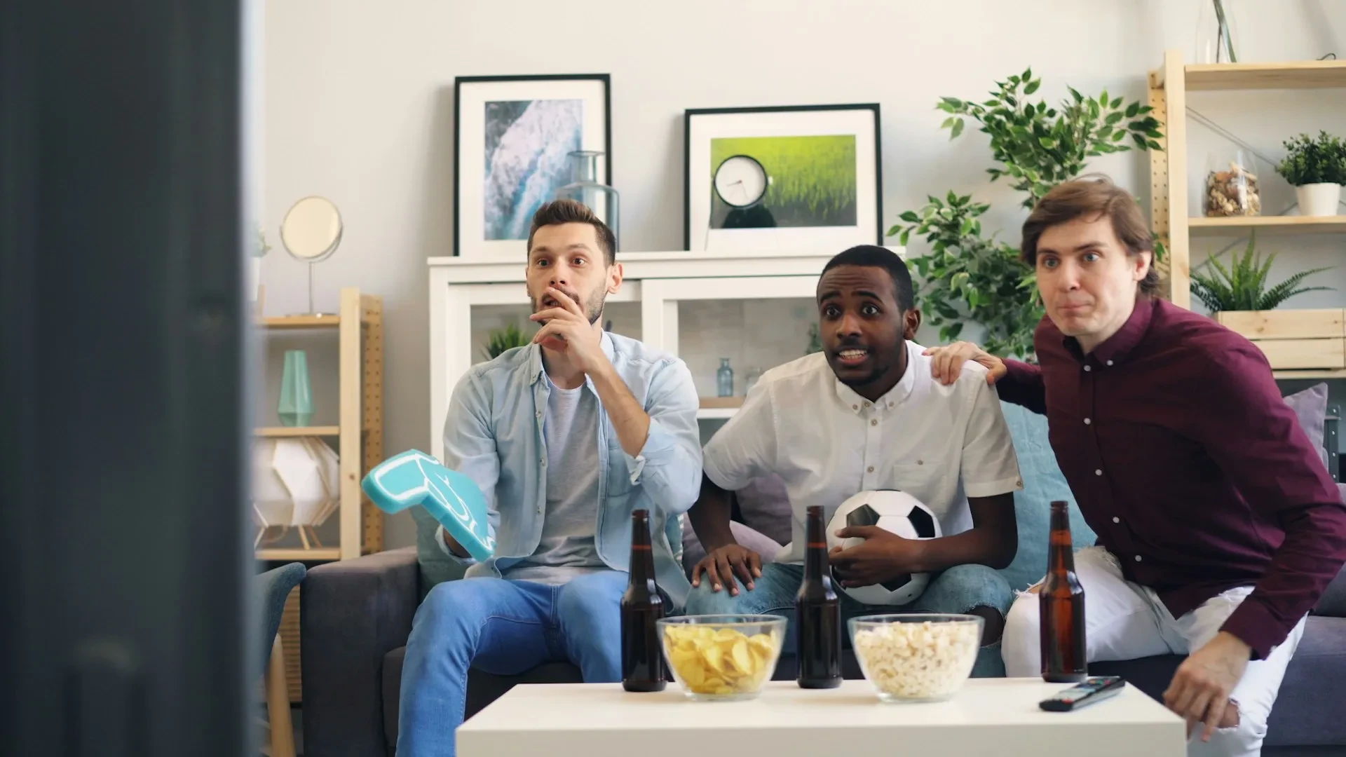 Three fans sit on their sofa watching and reaction to a match on their TV