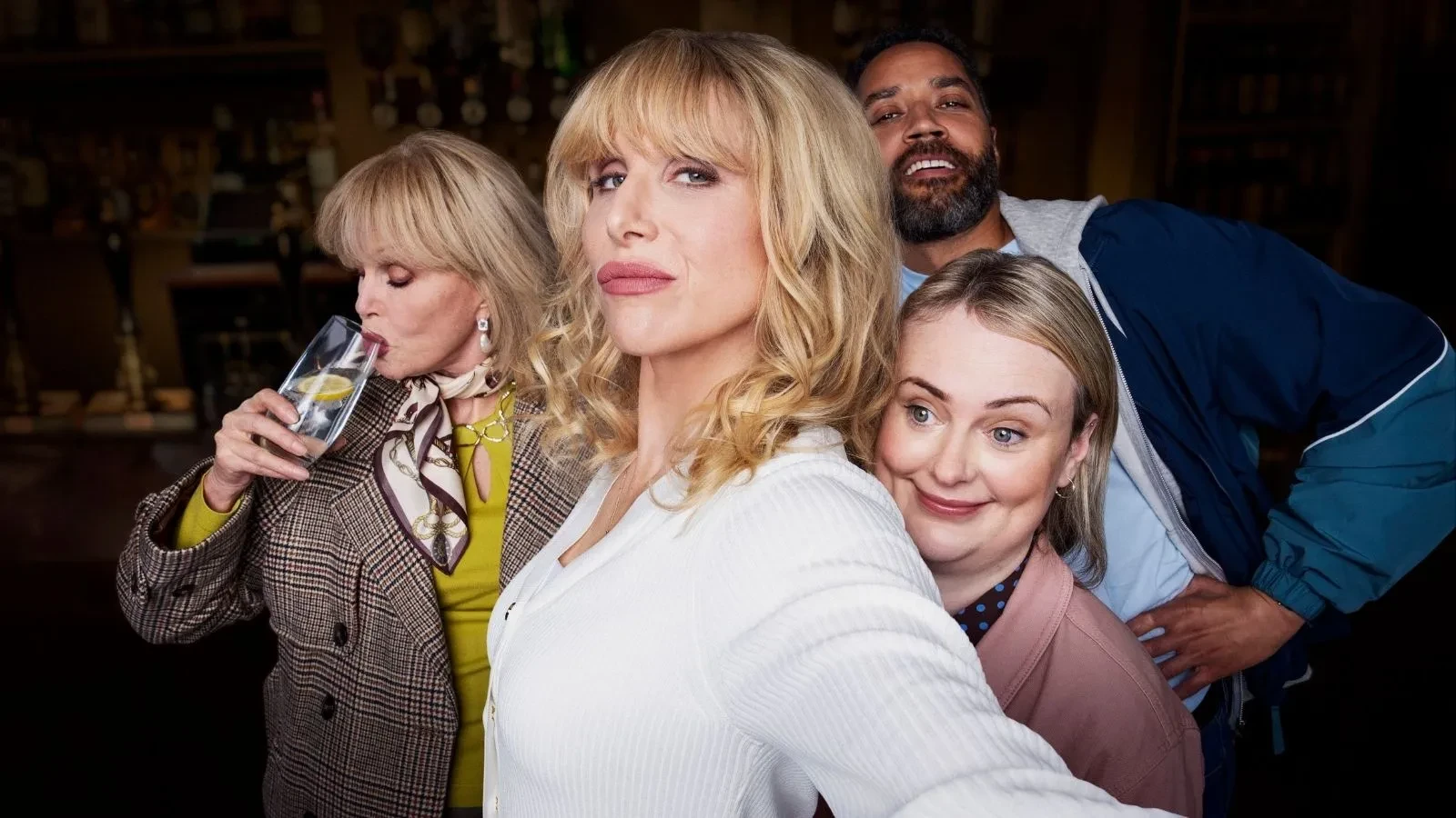 Television comedy drama promotional image showing four people standing together against a pastel blue background with floating decorative flowers.
