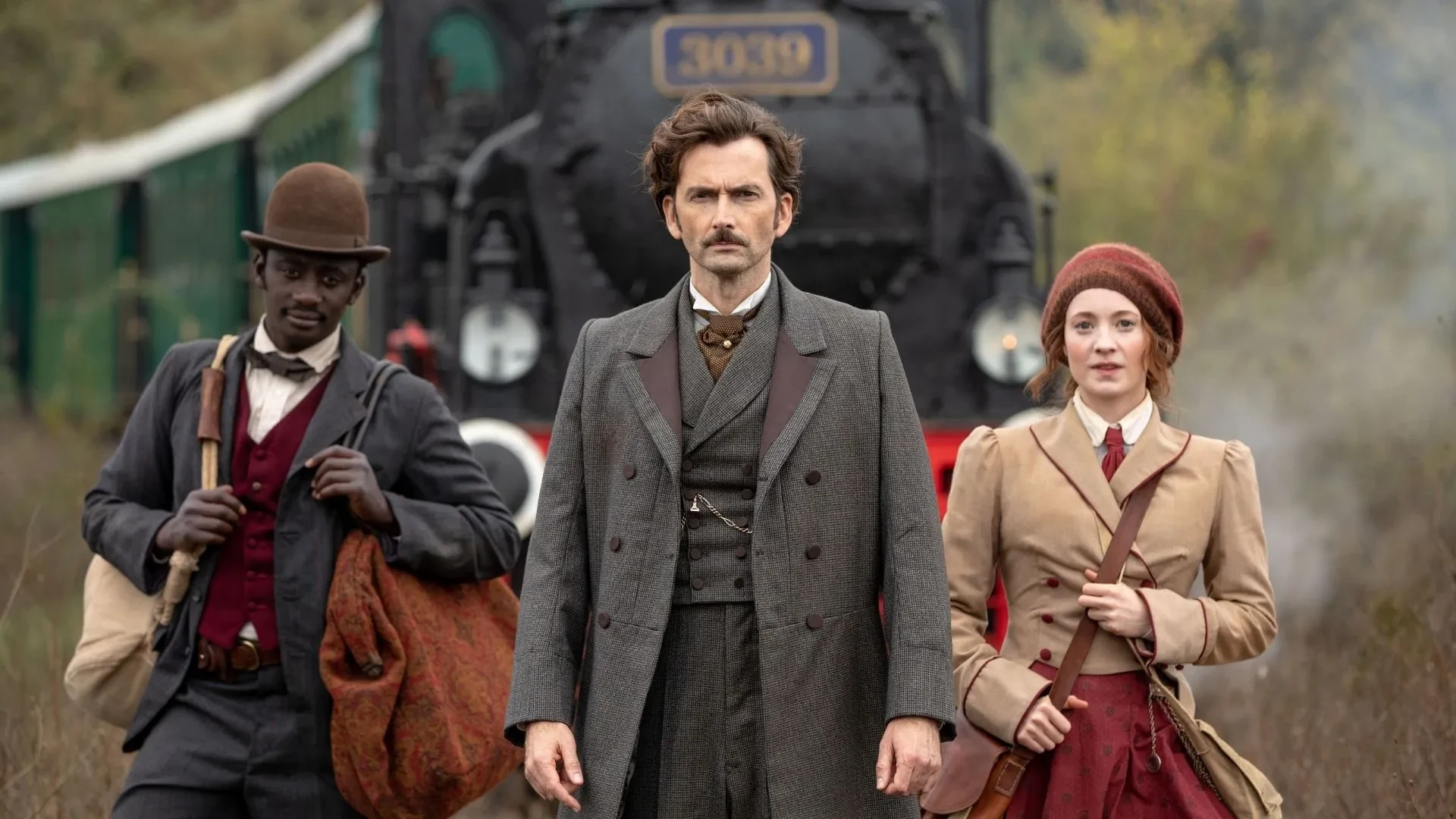 Period adventure drama scene from Around the World in 80 Days showing three travelers standing in front of a steam train.