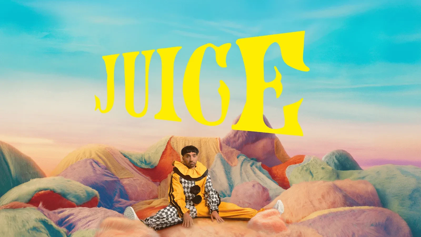 A man in a clown outfit sat on a landscape of blankets against a blue background with yellow writing that reads "Juice"