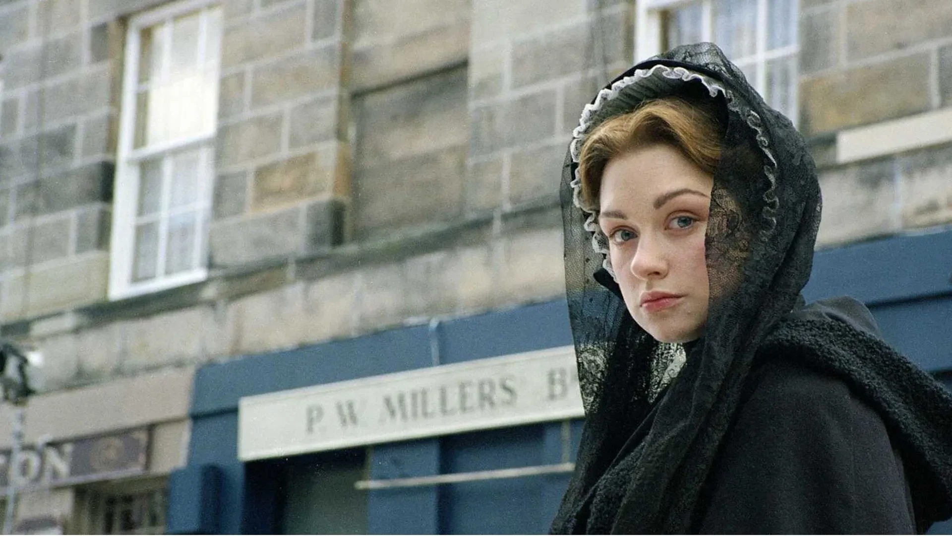 Victorian‑era period drama scene from North and South showing a character in black mourning clothing on a 19th‑century industrial street.