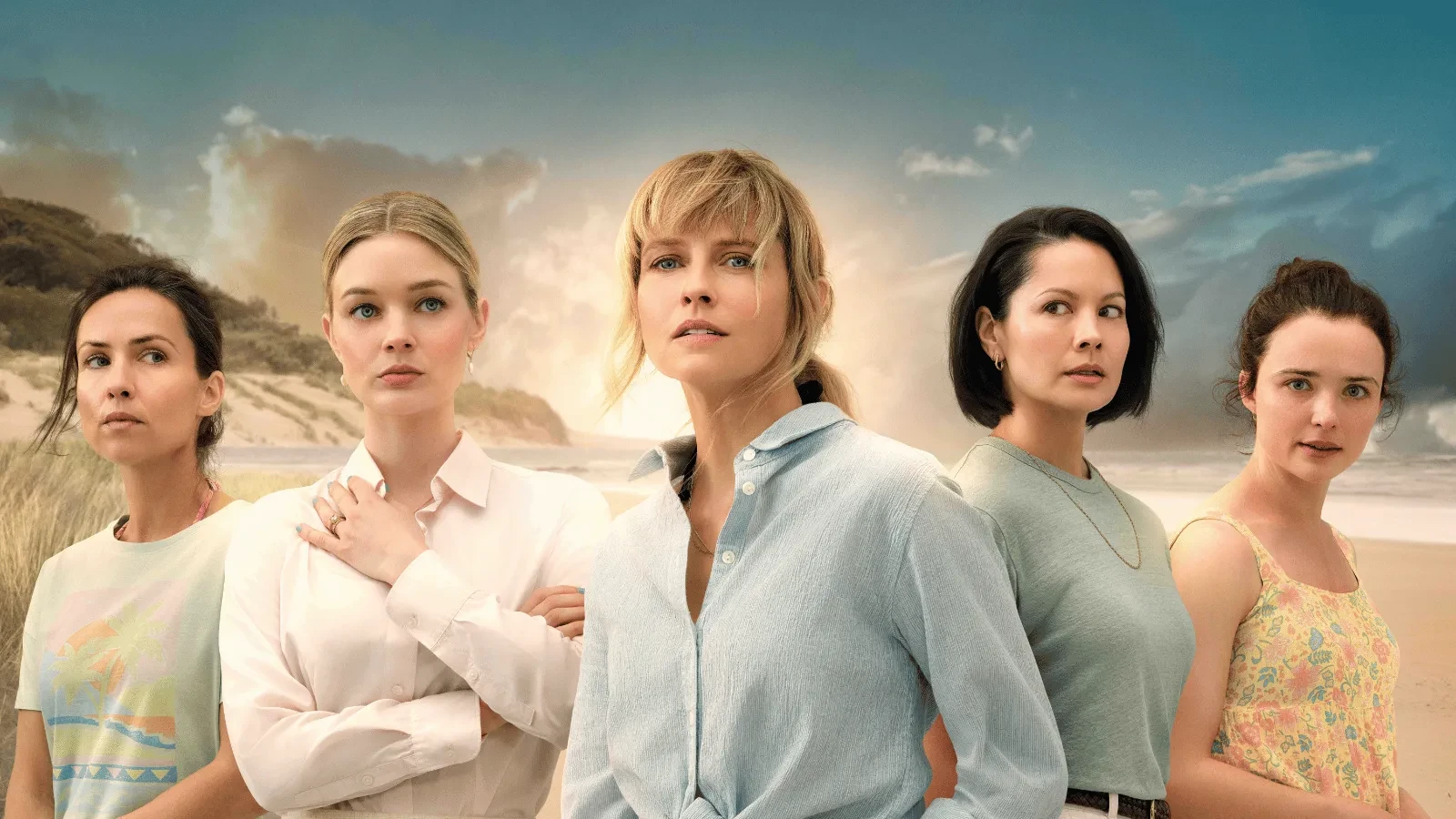 Five women wearing pale clothing stood looking suspiciously in different directions with a beach in the background