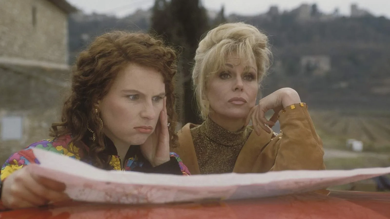 Two women in 80s clothing leaning on a car reading a map in the show Absolutely Fabulous