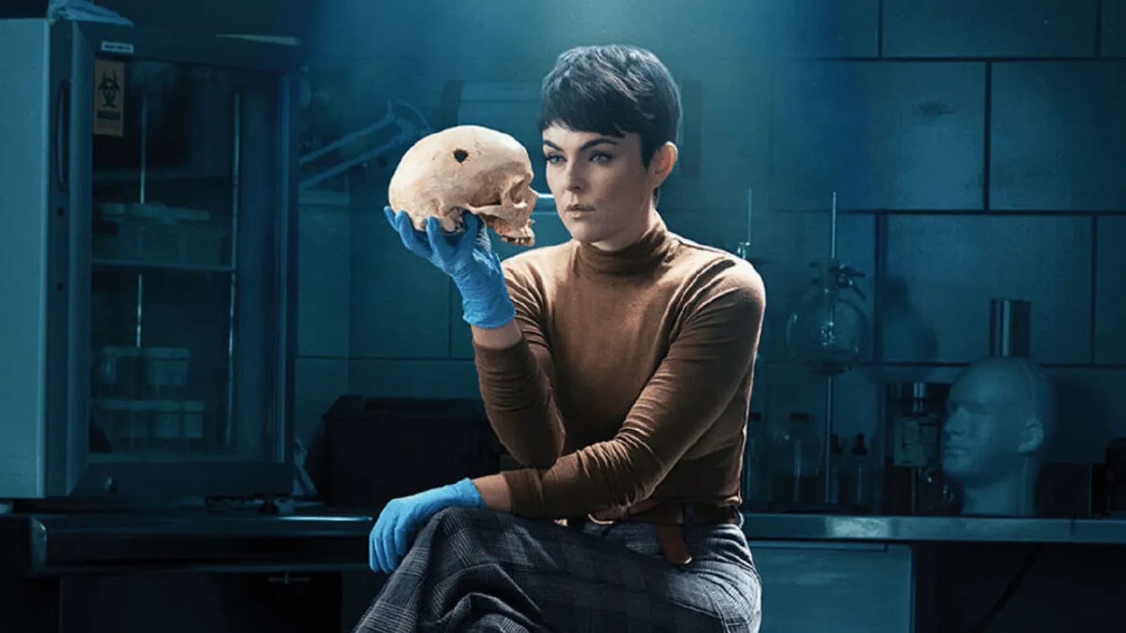 Crime drama scene from Coroner showing a forensic investigator in a laboratory examining a human skull while wearing blue protective gloves.
