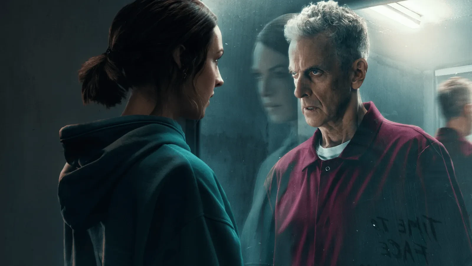 A woman wearing a grey hoodie stood looking at a man in a red jumpsuit through glass.
