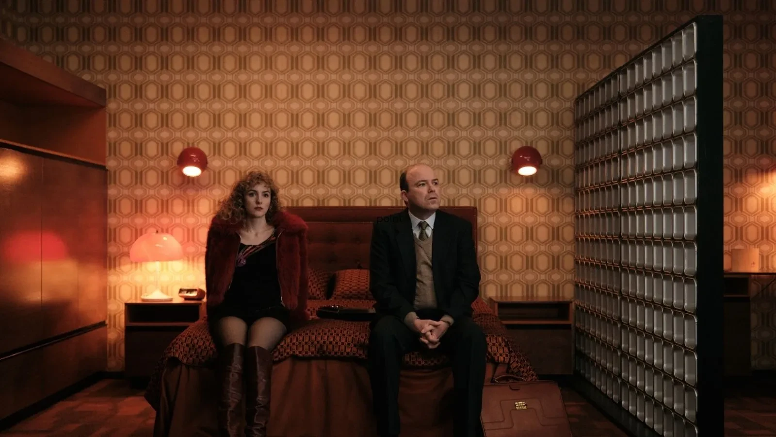 Copilot said: Honey promotional image featuring two people seated on a bed in a retro-style hotel room, surrounded by warm amber lighting, geometric patterned wallpaper and vintage furnishings, highlighting themes of mystery, suspense and interpersonal drama in a stylish period setting.