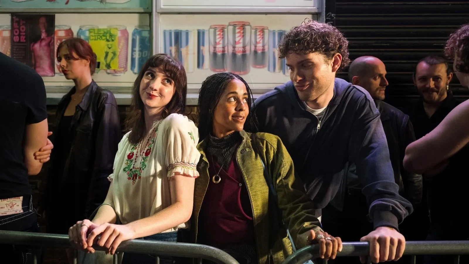 Copilot said: It Gets Worse promotional image featuring three people leaning against a crowd barrier at a lively nightlife venue, surrounded by colourful posters, drinks advertisements and onlookers, highlighting themes of friendship, romance, comedy and modern social life in a vibrant urban setting.