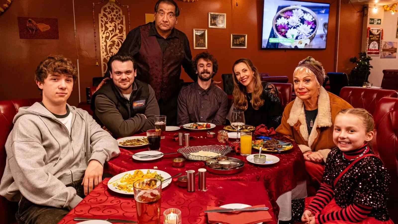 Copilot said: Stepping Up promotional image featuring a group gathered around a restaurant dining table surrounded by plates of food and drinks, set within a warmly lit venue with colourful décor, highlighting themes of family life, community, humour and contemporary drama.