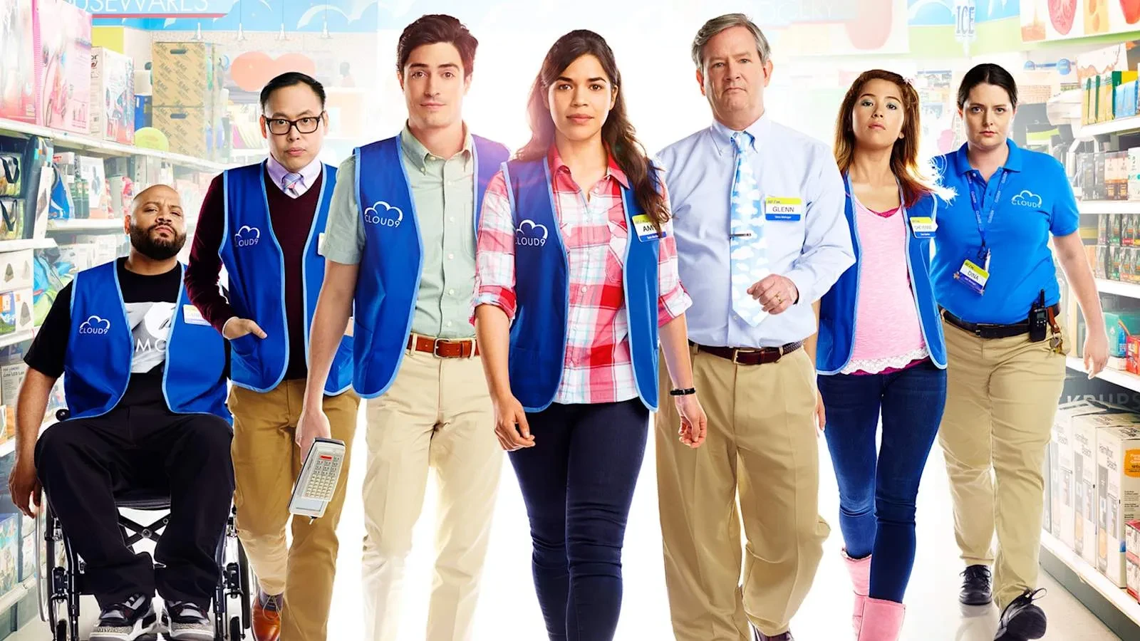 A group of retail employees wearing blue store vests walk through a supermarket aisle toward the camera. The diverse team is featured in a bright promotional image that highlights the workplace comedy setting.