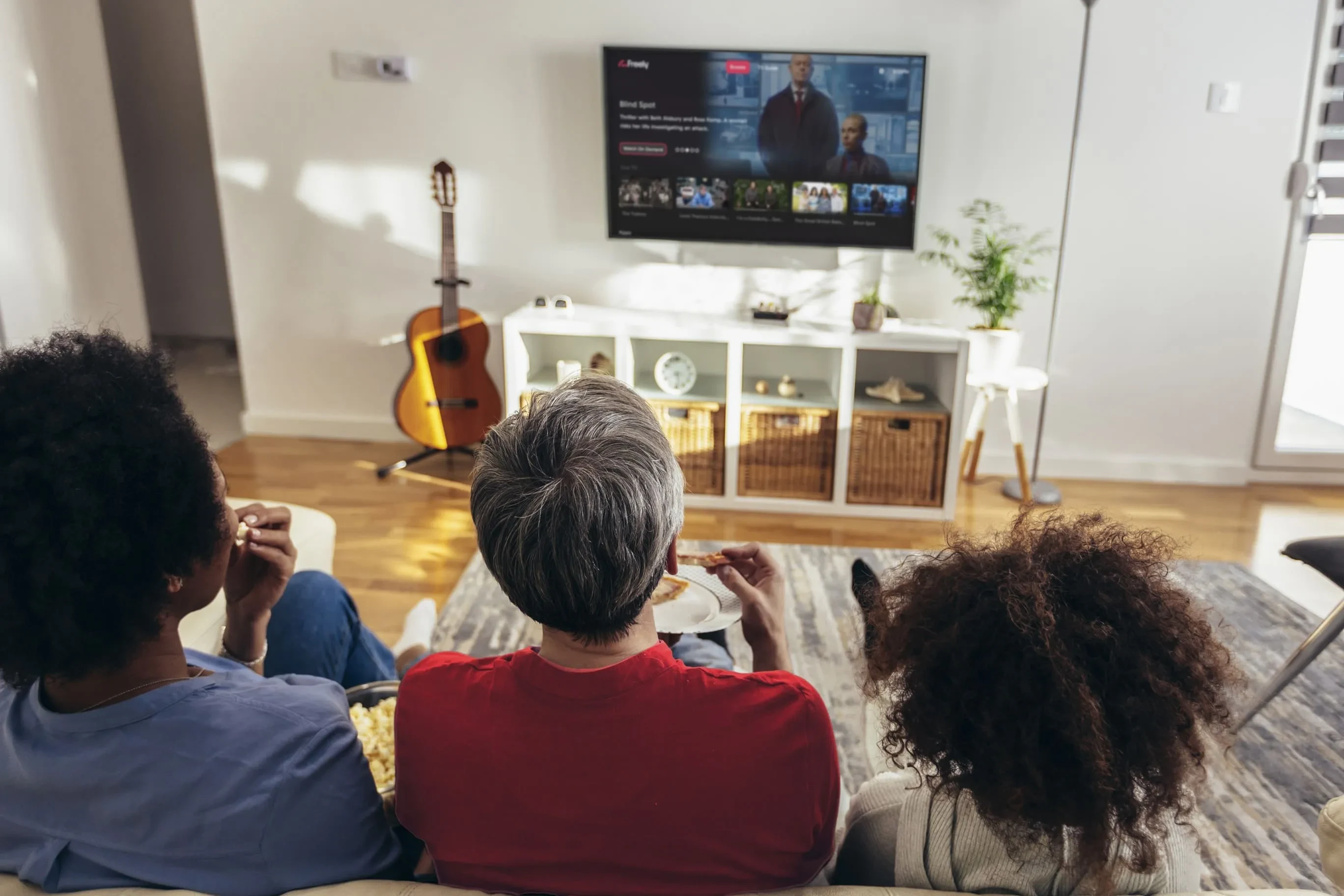 Three people sit watching a Freely TV in their living room