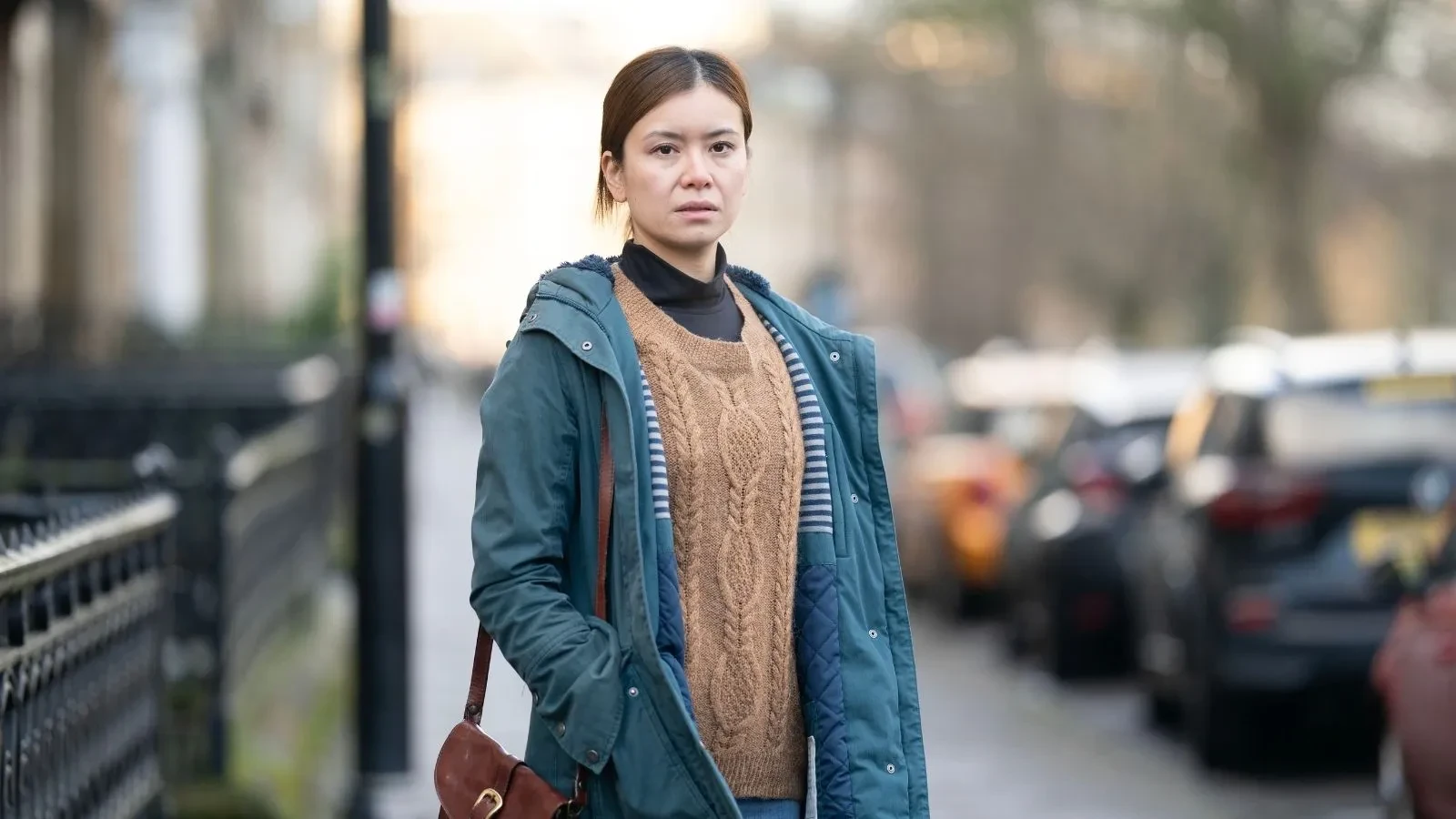 Katie Leung wearing a blue jacket and yellow jumper stood in the street in the new channel 4 drama Careless