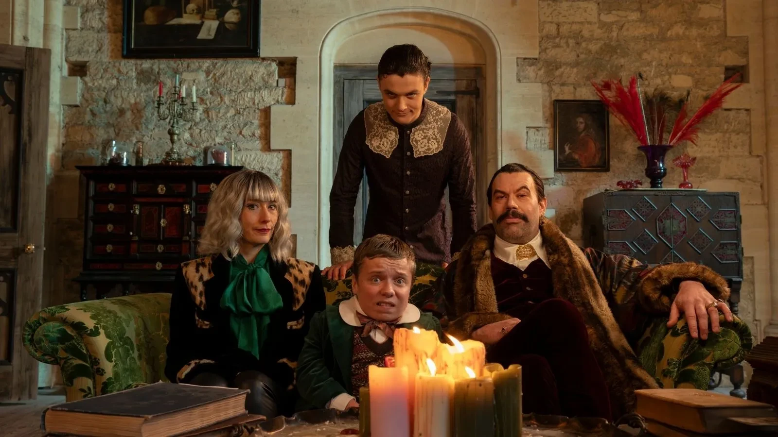 Two adults and two teenagers dressed in medieval clothing in a castle looking into the camera. Key art for the BBC show the reluctant vampire.