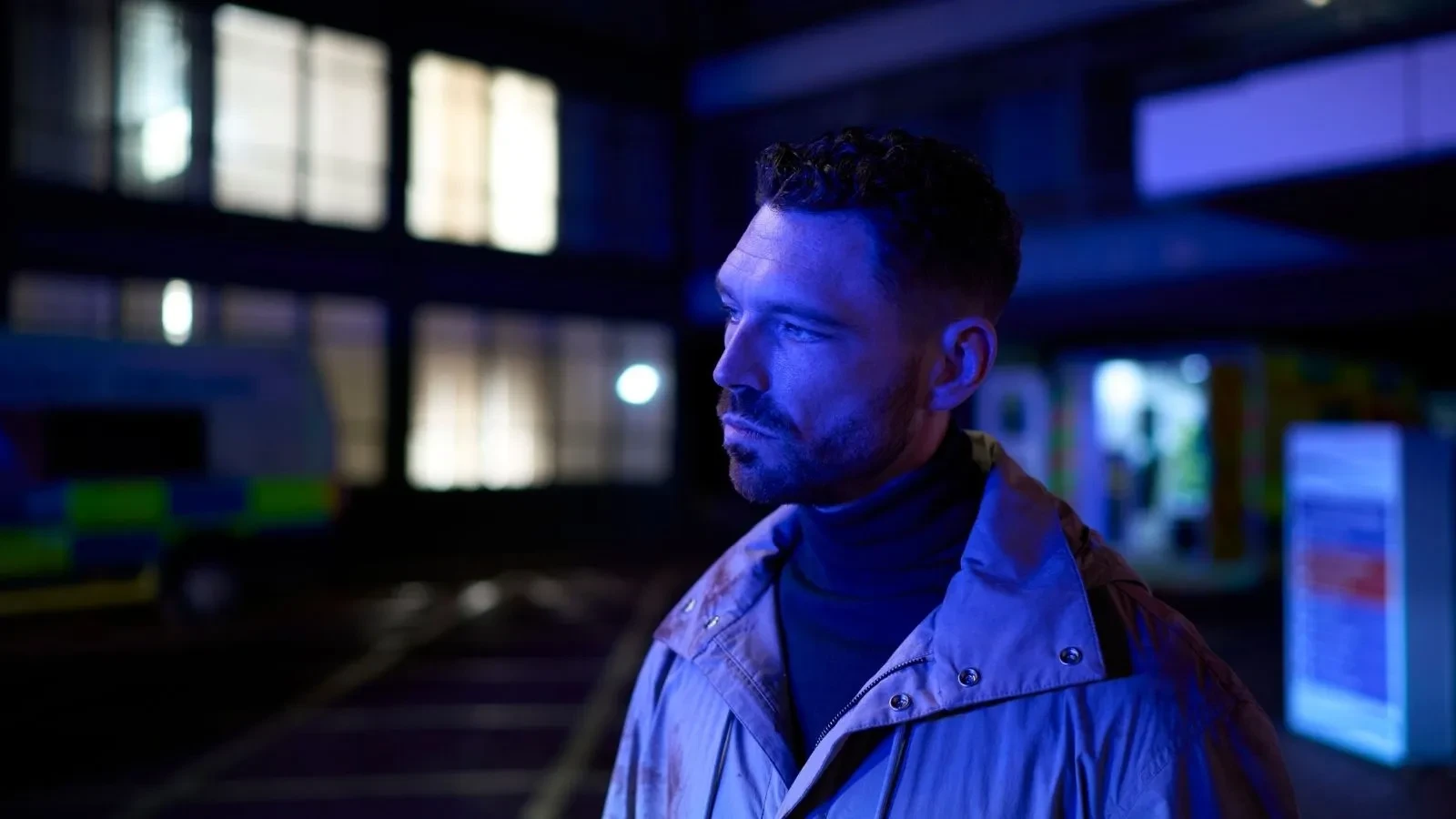 A man in a white jacket in blue faded light stood in front of a building