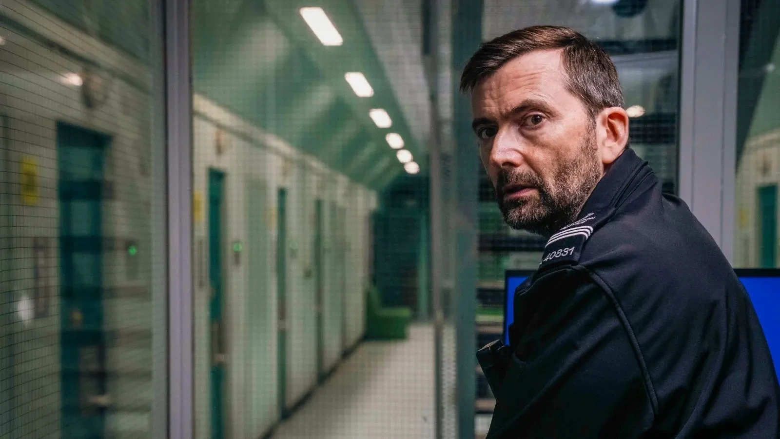 David Tennant in season 3 of time stood wearing prison uniform over looking a prison