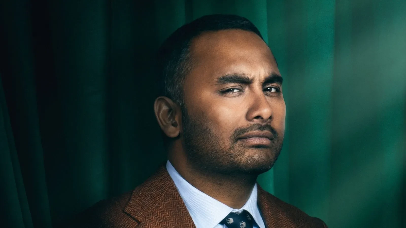 Amol Rajan stood against a green backdrop in Celebrity Traitors