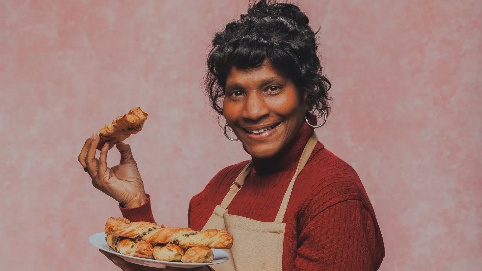 Great British Bake Off baker Connie holding a plate of freshly baked chocolate pastries in a studio portrait.