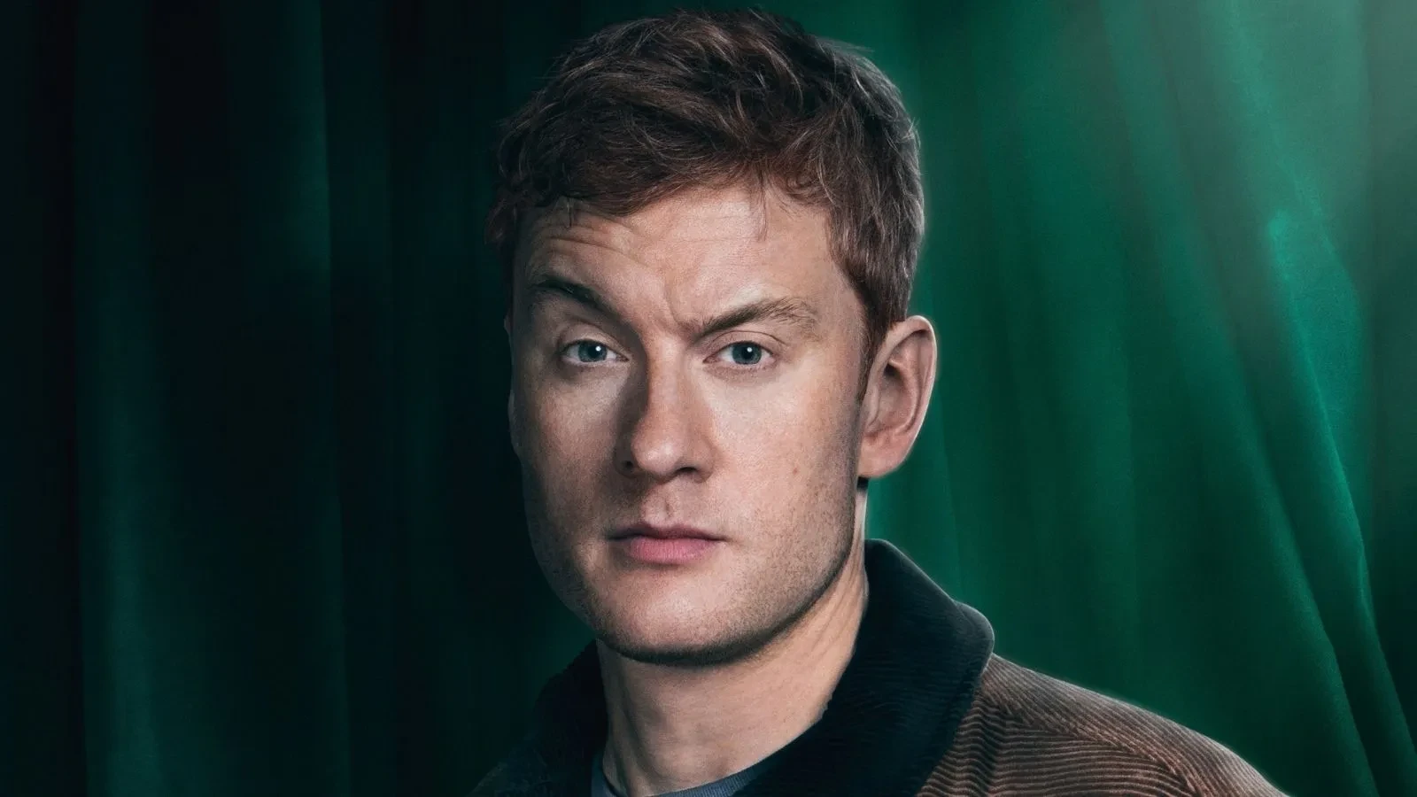 James Acaster stood against a green backdrop in Celebrity Traitors