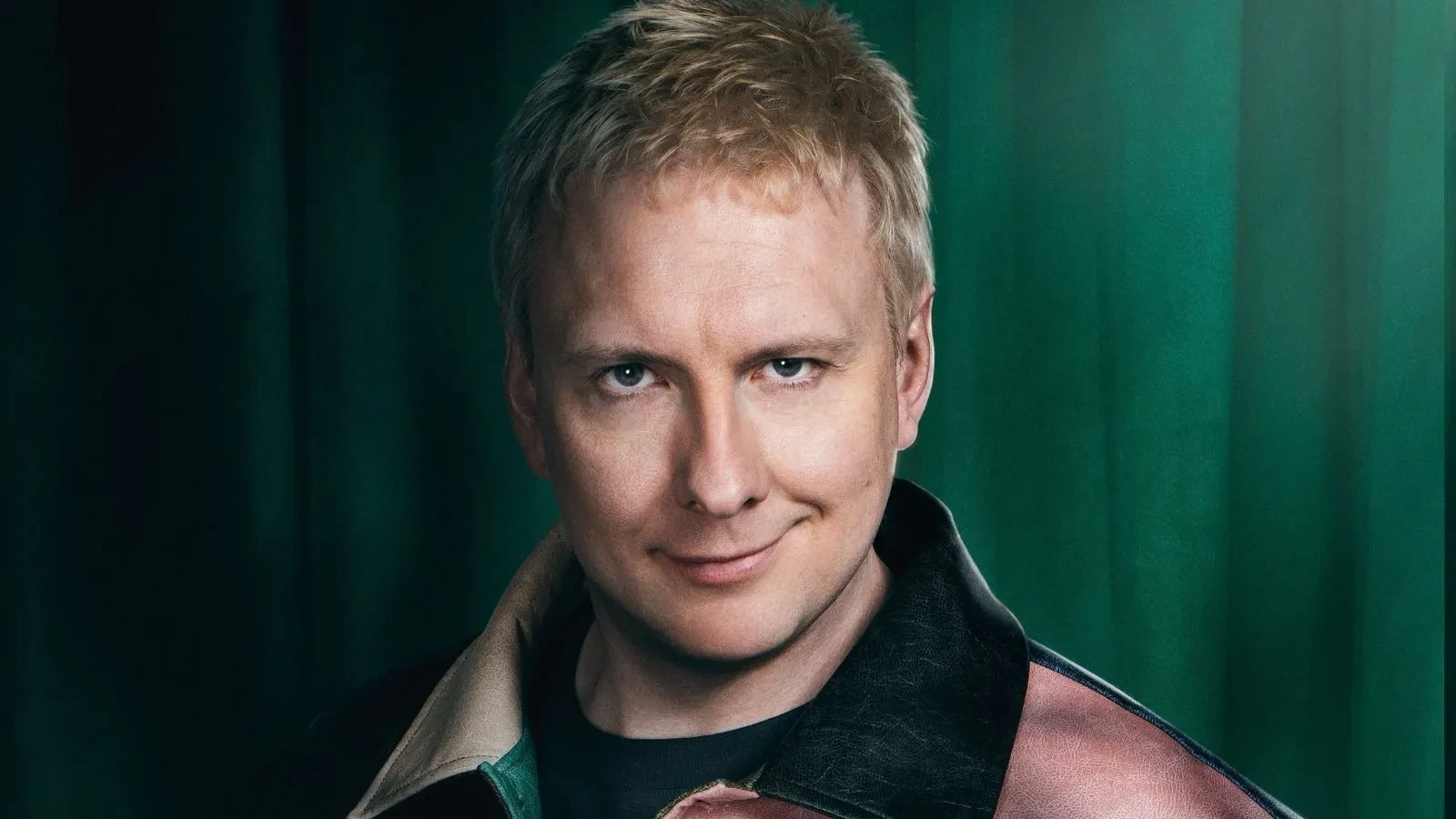 Joe Lycett stood against a green backdrop in Celebrity Traitors