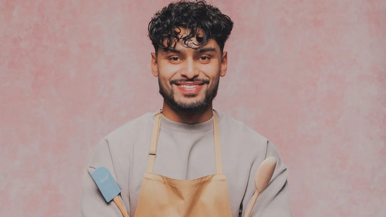 Great British Bake Off baker Mo holding baking utensils in an official GBBO contestant portrait.