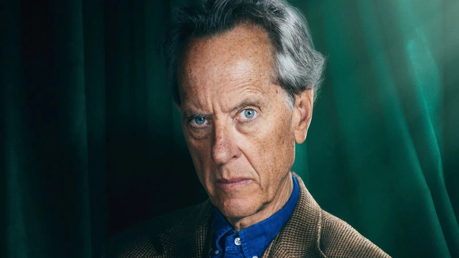 Richard E. Grant stood against a green background in Celebrity Traitors