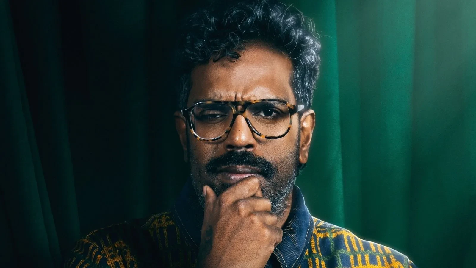 Romesh Ranganathan stood against a green background in Celebrity Traitors