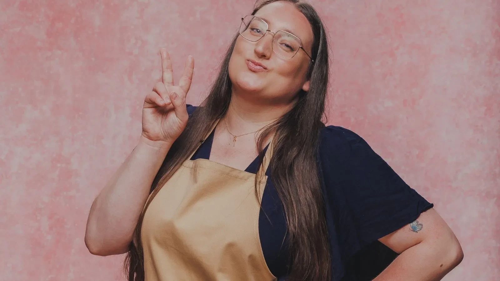 Great British Bake Off baker Shannon wearing a baking apron and making a peace sign in an official GBBO contestant portrait.