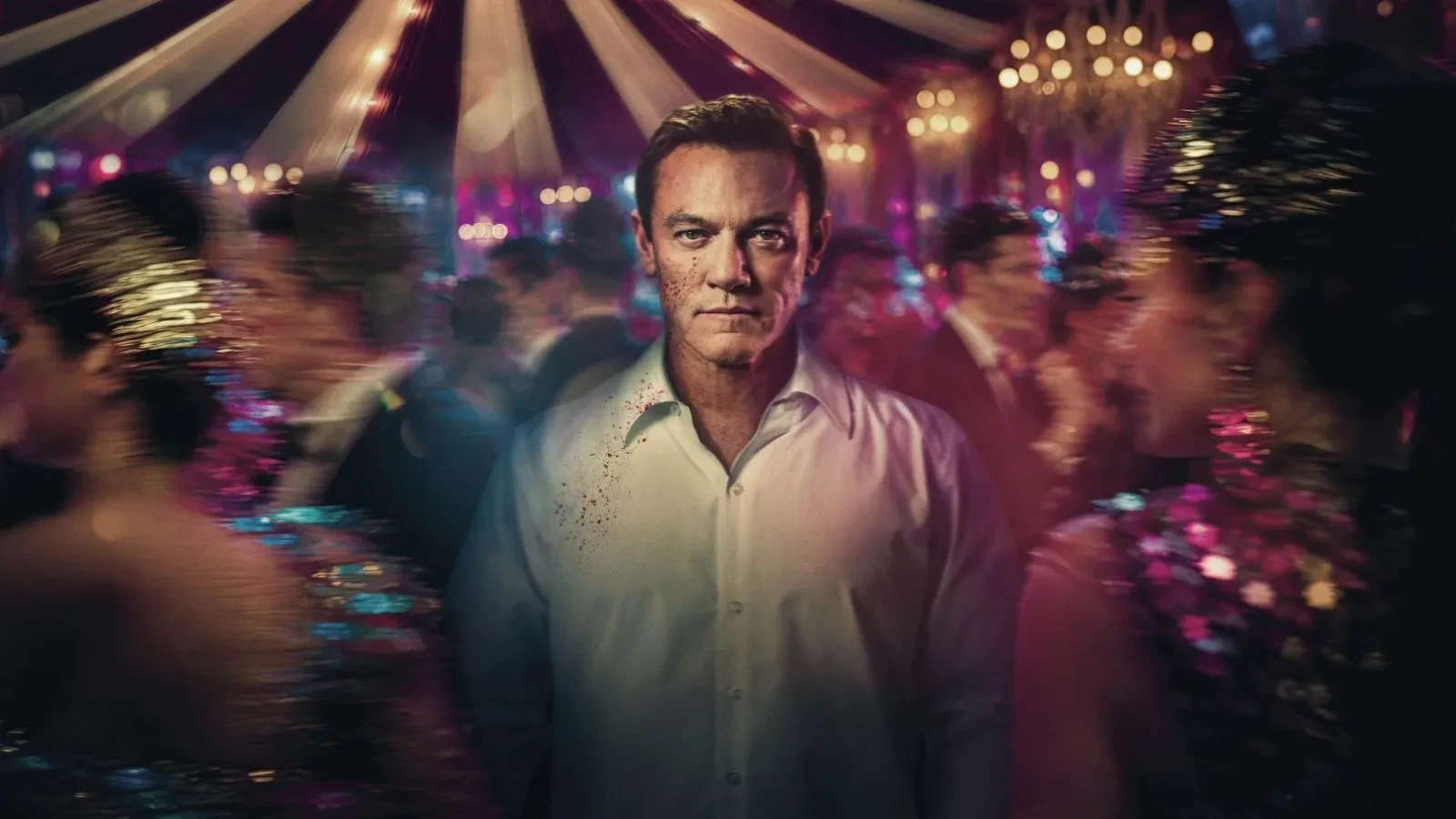 Luke Evans stood in the middle of a crowded scene with a circus tent in the background in the drama The Party