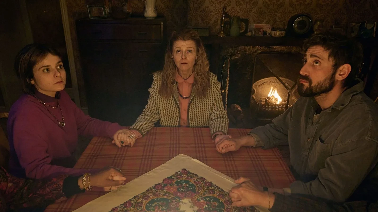 Family members gather around a table during a tense séance scene in supernatural drama Witch Farm.