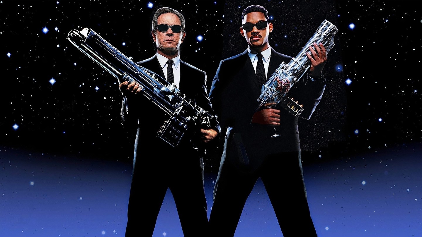 Two men i suits with sunglasses holding intergalactic style weapons 