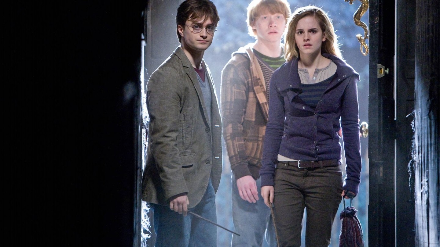 Three characters enter a dark doorway with mist behind them, holding a wand and a broomstick. Scene from Harry Potter and the Deathly Hallows: Part 2
