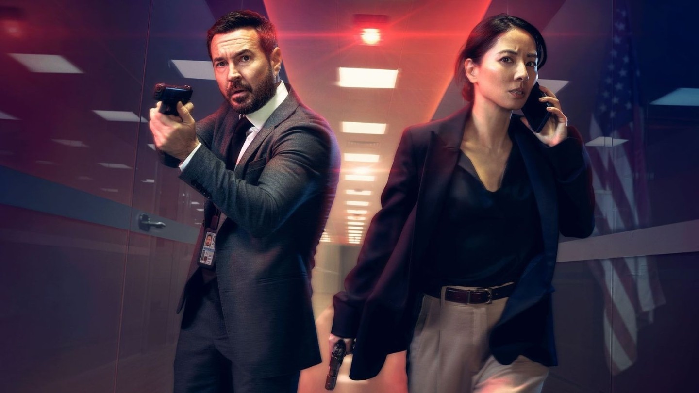 Promotional art from season 2 of the British drama series Red Eye, showing two suited figures in a sleek, brightly lit corridor with red overhead lights. Both are holding guns, and one is speaking on a mobile phone.