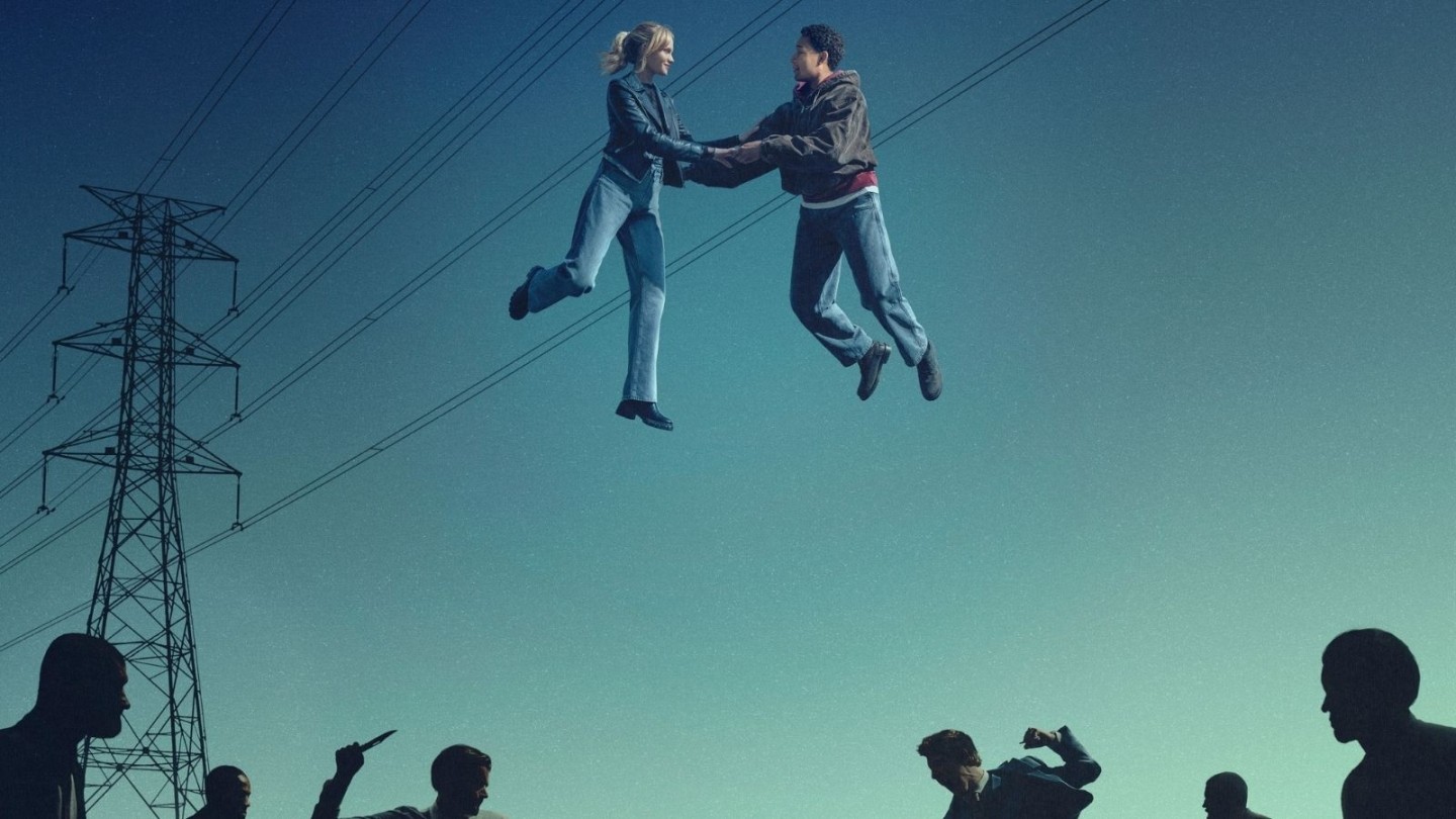Two people suspended mid‑air while holding hands above a group of silhouetted figures, set against a clear sky with electricity pylons and overhead power lines in the background.