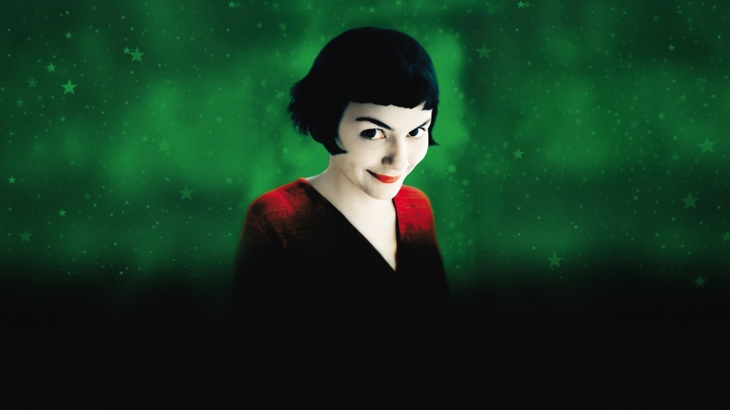 Promotional image for Amelie, pale woman with dark hair smiling at the camera against a dark green background