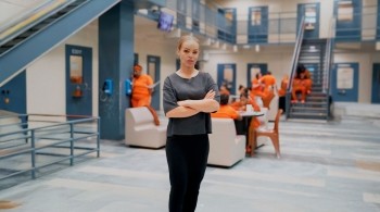Katie Piper Stood in a prison with inmates in orange jumpsuits in the background