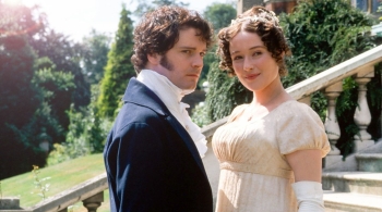 Still image from the 1995 TV series Pride & Prejudice showing a man and woman in Regency-era dress standing on stone steps outdoors, with trees and a country garden behind them.